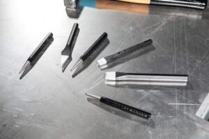 Multifunktionales Werkzeugset mit 6 Teilen, bestehend aus Meißeln, Durchtriebern und Körnern, gefertigt aus Chrom-Vanadium-Stahl und befestigt in Kunststoffständern.